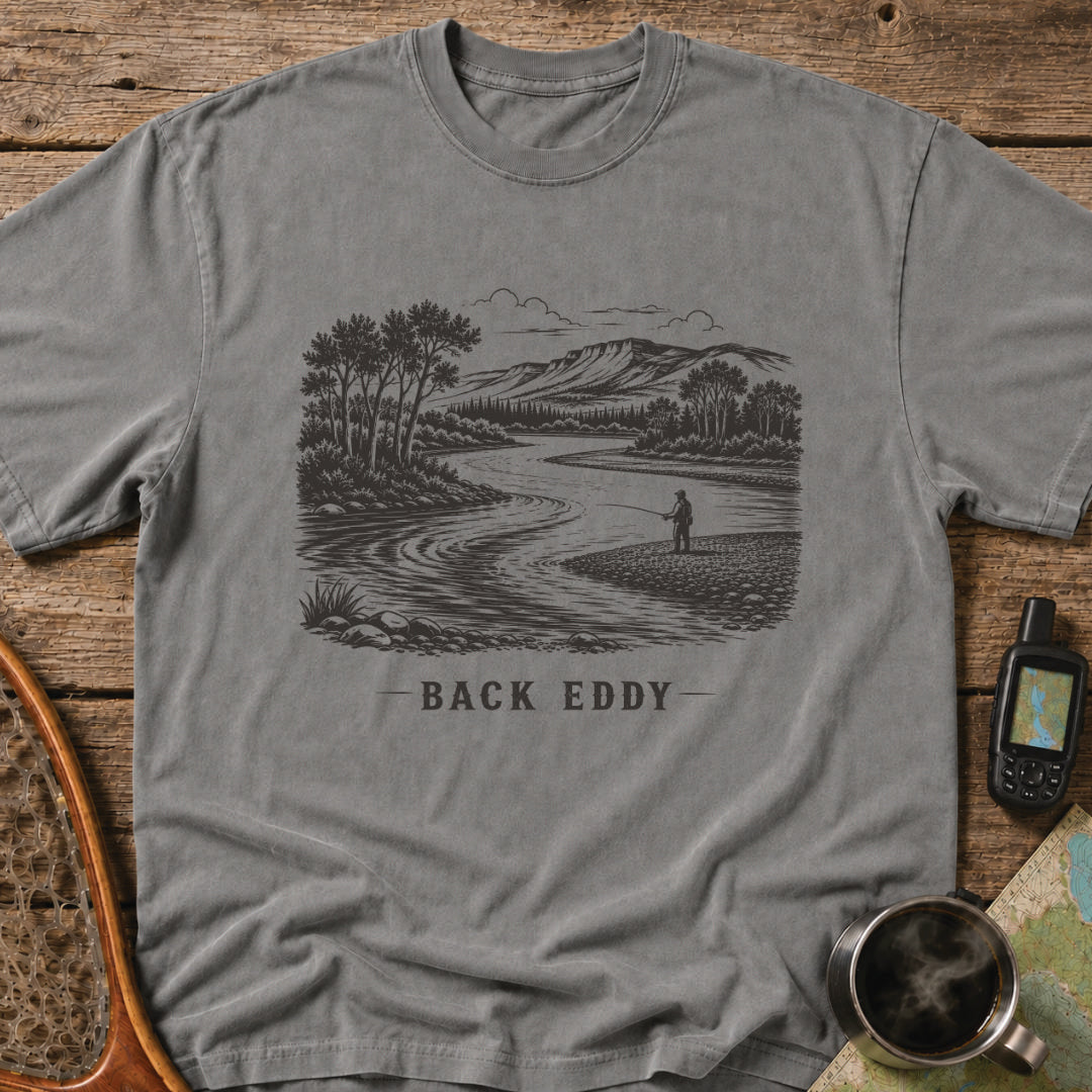 Fly fishing t-shirt featuring an engraved river landscape with a lone angler standing in a back eddy beneath mountain scenery.