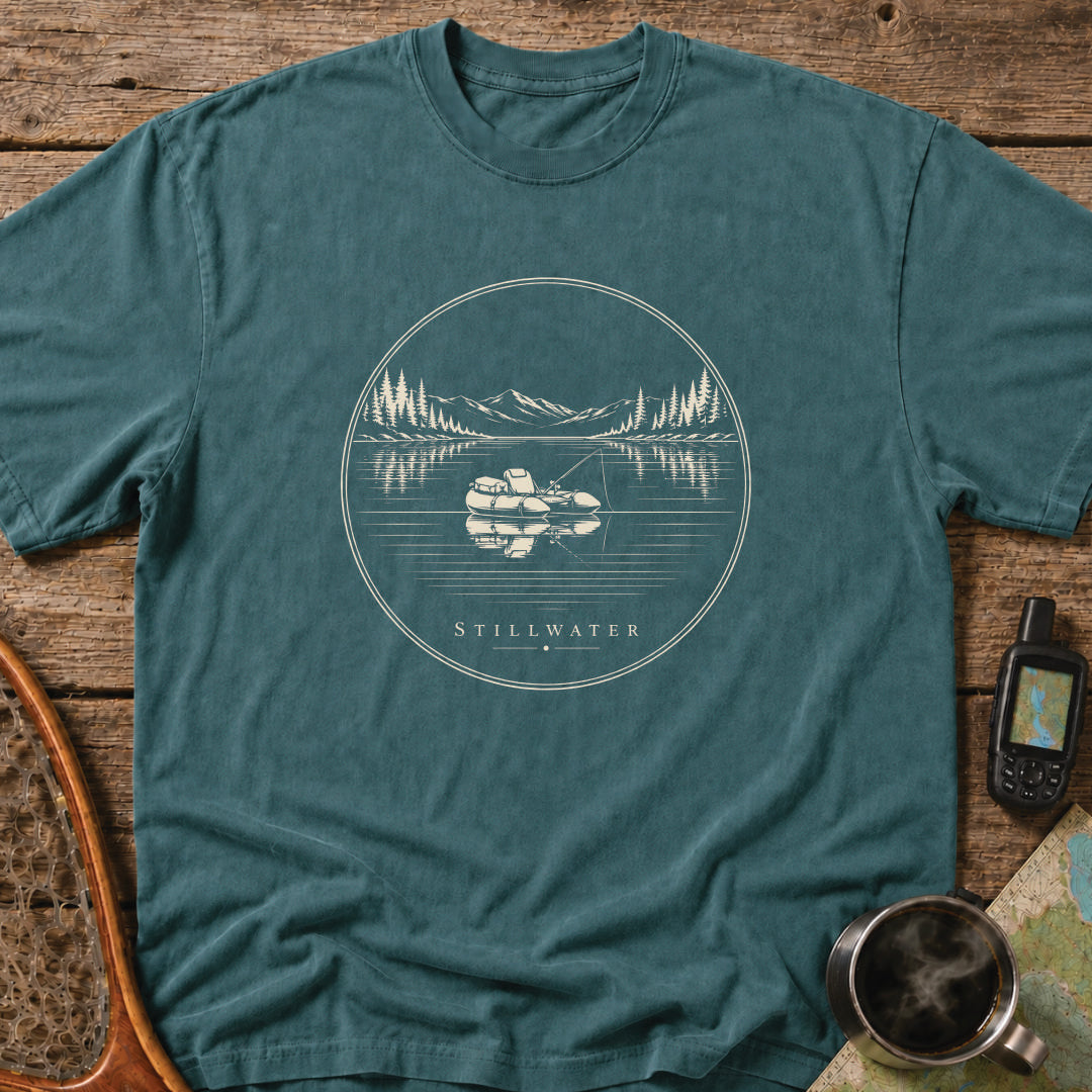 Stillwater t-shirt featuring a packraft floating on a calm mountain lake at sunset.