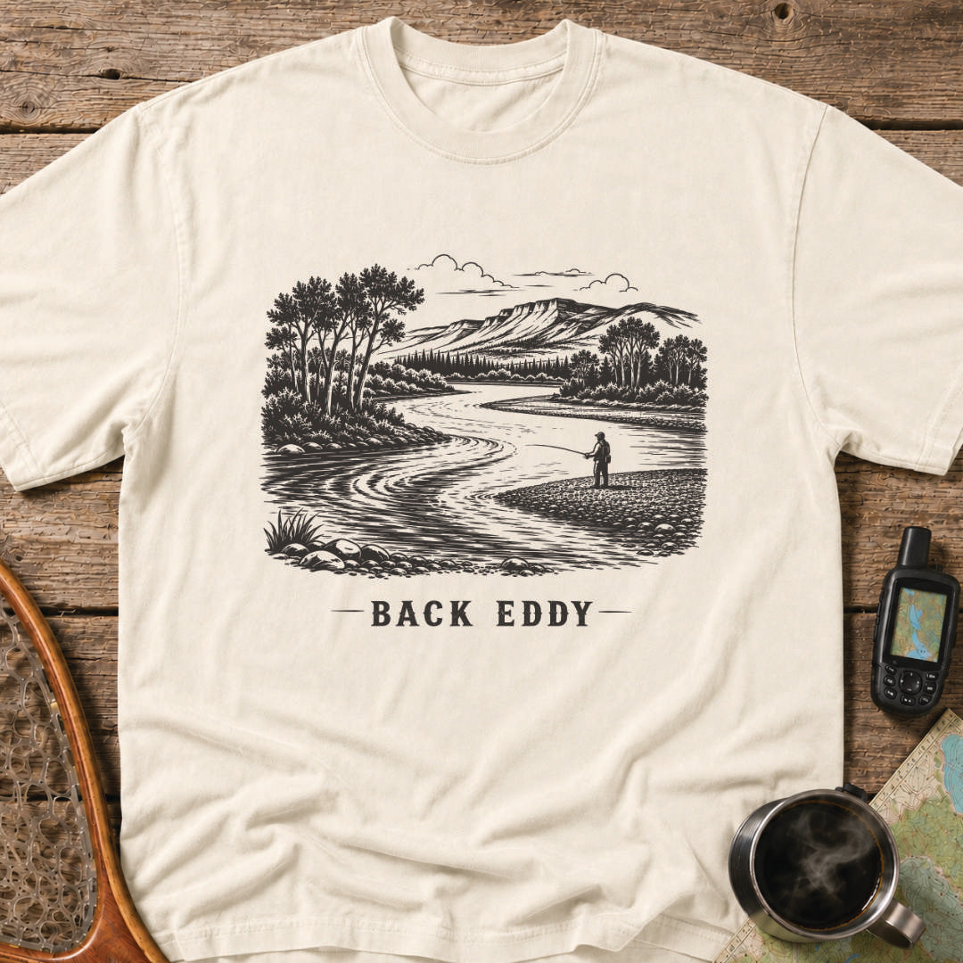 Fly fishing t-shirt featuring an engraved river landscape with a lone angler standing in a back eddy beneath mountain scenery.