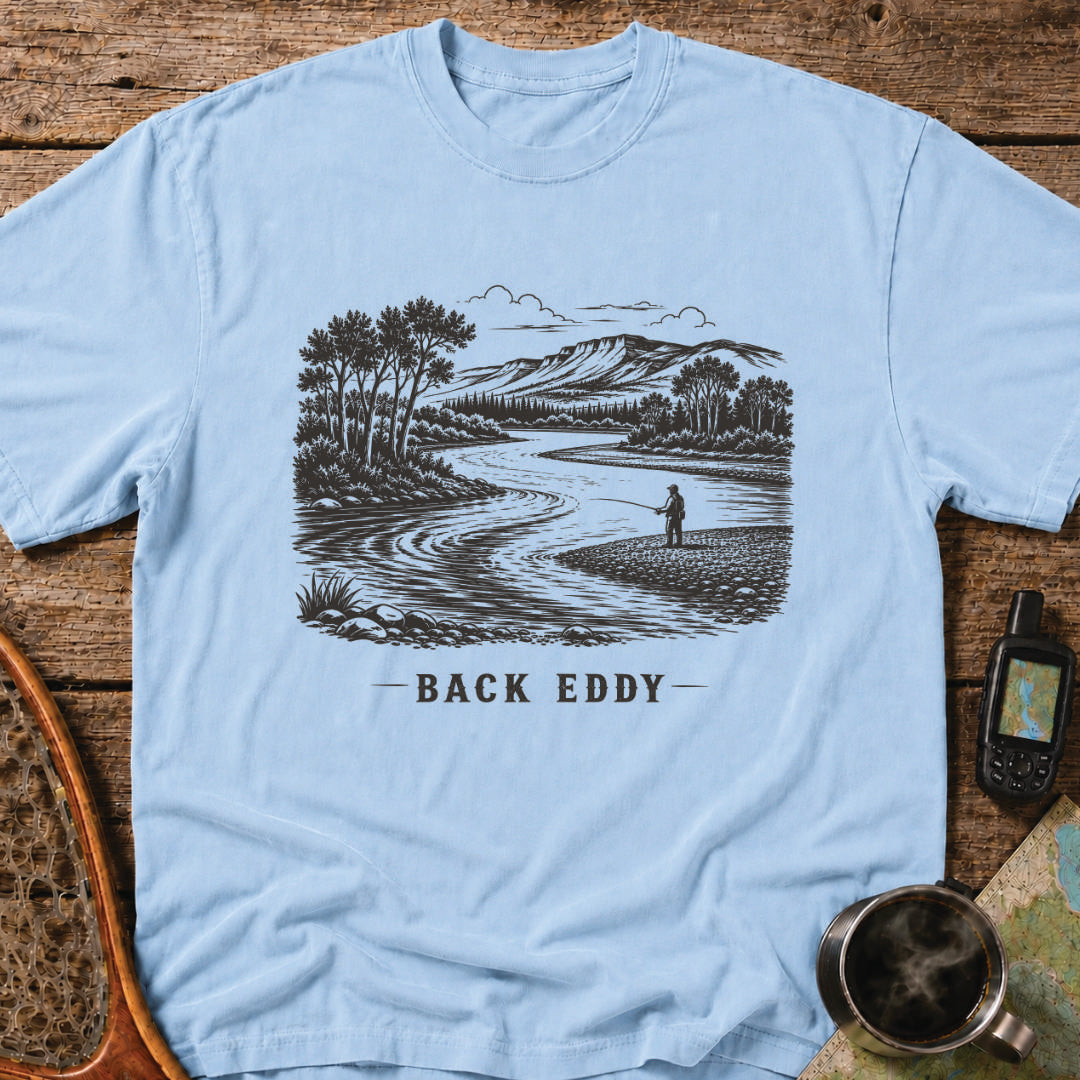 Fly fishing t-shirt featuring an engraved river landscape with a lone angler standing in a back eddy beneath mountain scenery.
