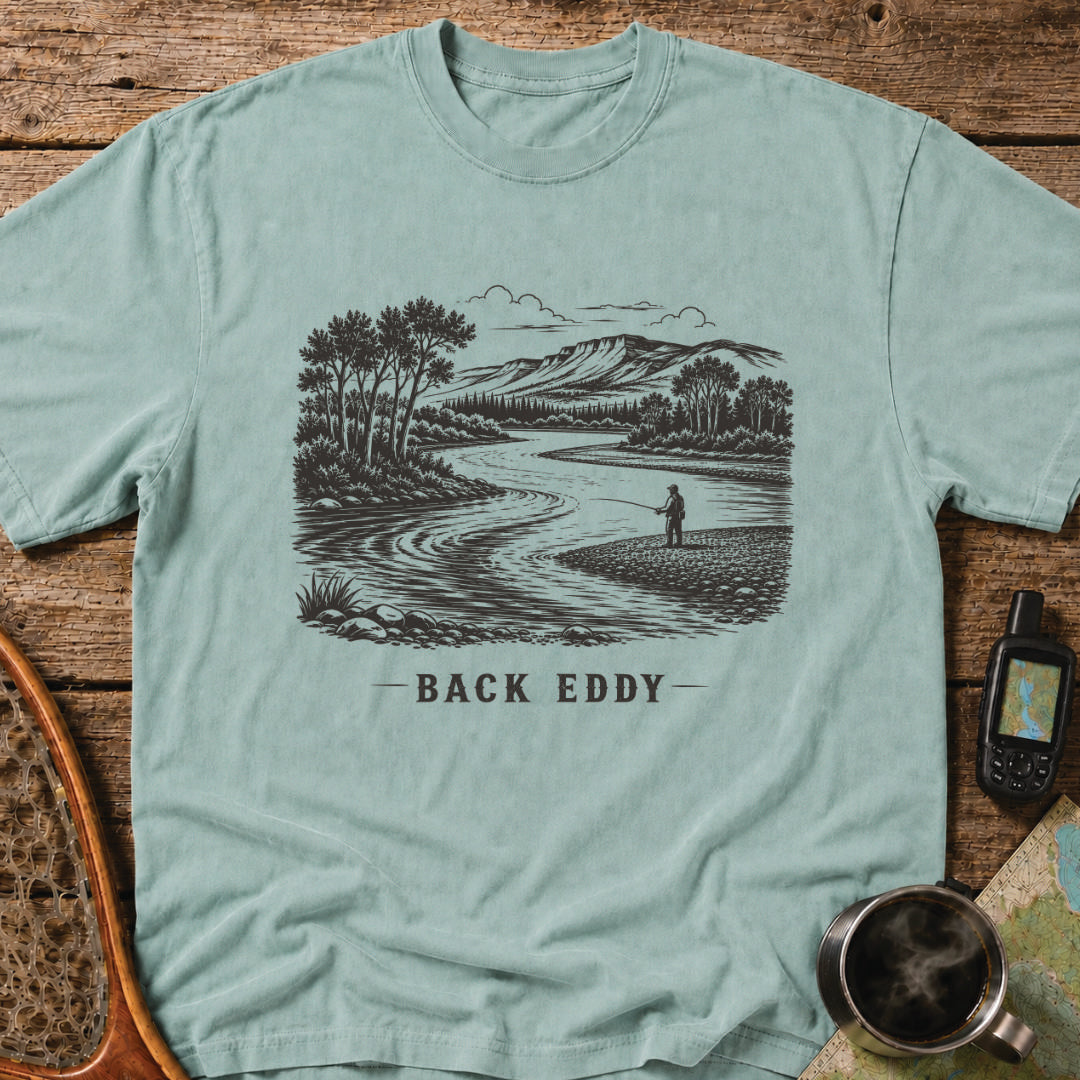 Fly fishing t-shirt featuring an engraved river landscape with a lone angler standing in a back eddy beneath mountain scenery.