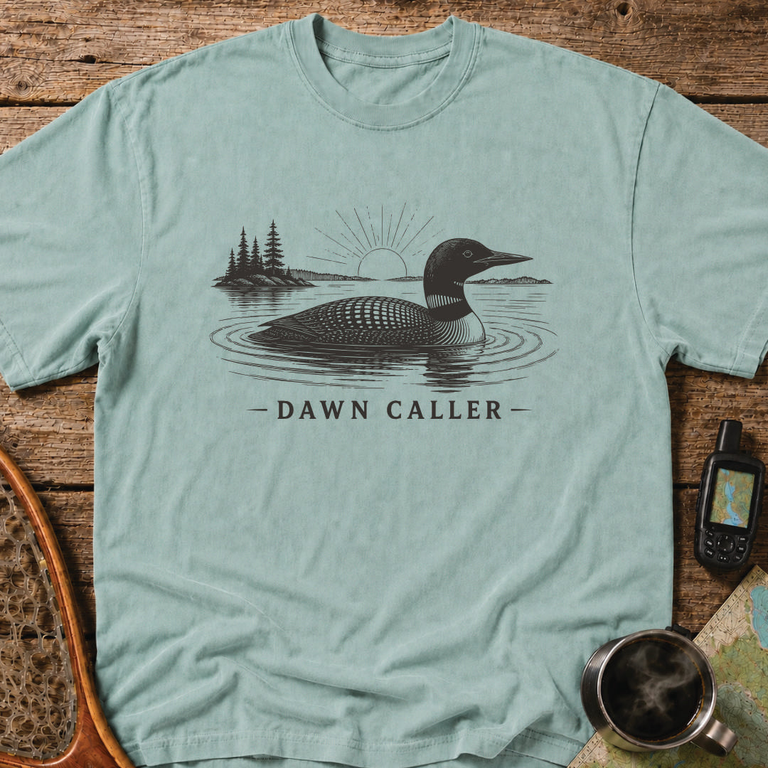 Dawn Caller loon t-shirt featuring a detailed loon floating on a northern lake at sunrise with wilderness shoreline artwork.