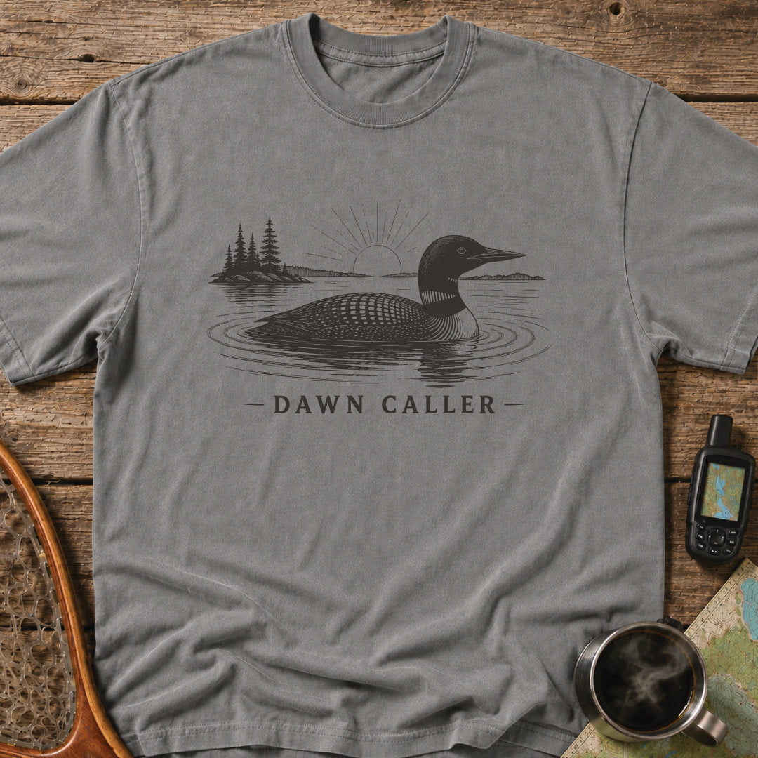 Dawn Caller loon t-shirt featuring a detailed loon floating on a northern lake at sunrise with wilderness shoreline artwork.