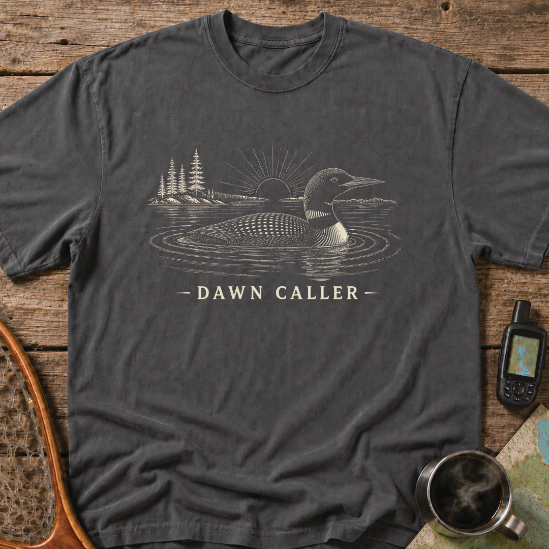 Dawn Caller loon t-shirt featuring a detailed loon floating on a northern lake at sunrise with wilderness shoreline artwork.