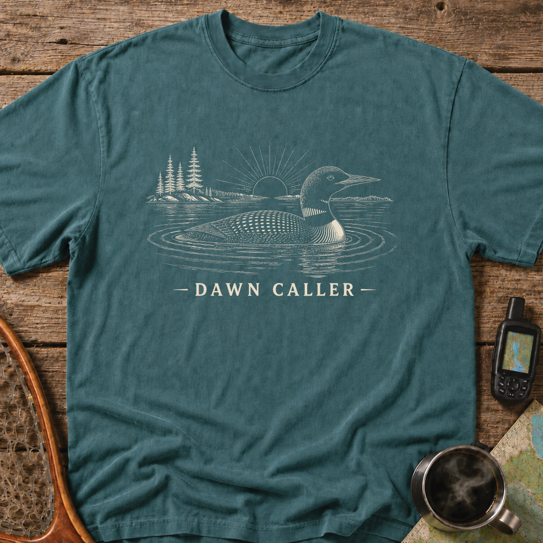 Dawn Caller loon t-shirt featuring a detailed loon floating on a northern lake at sunrise with wilderness shoreline artwork.