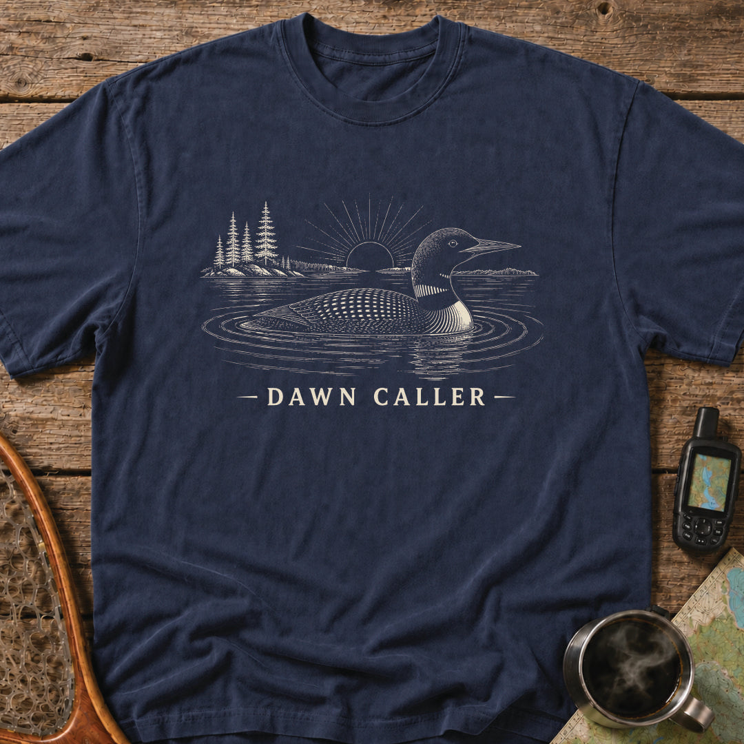Dawn Caller loon t-shirt featuring a detailed loon floating on a northern lake at sunrise with wilderness shoreline artwork.