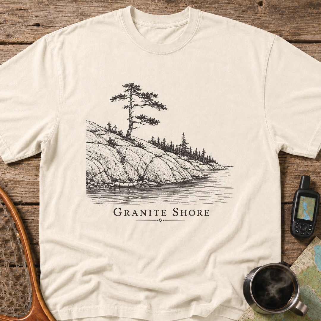 Granite Shore t-shirt featuring a rocky northern shoreline with pine trees overlooking calm wilderness water.