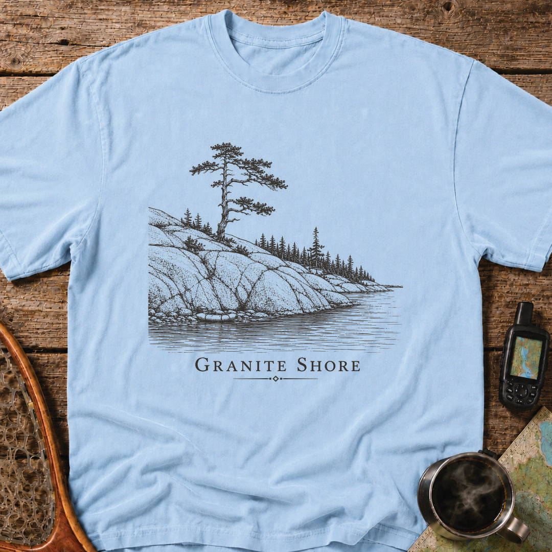 Granite Shore t-shirt featuring a rocky northern shoreline with pine trees overlooking calm wilderness water.
