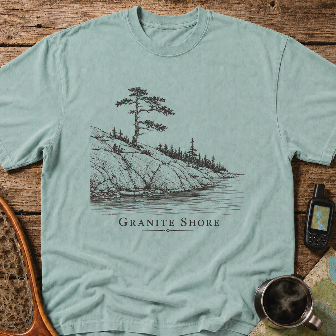 Granite Shore t-shirt featuring a rocky northern shoreline with pine trees overlooking calm wilderness water.