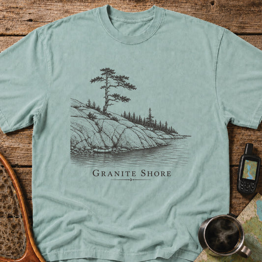Granite Shore t-shirt featuring a rocky northern shoreline with pine trees overlooking calm wilderness water.