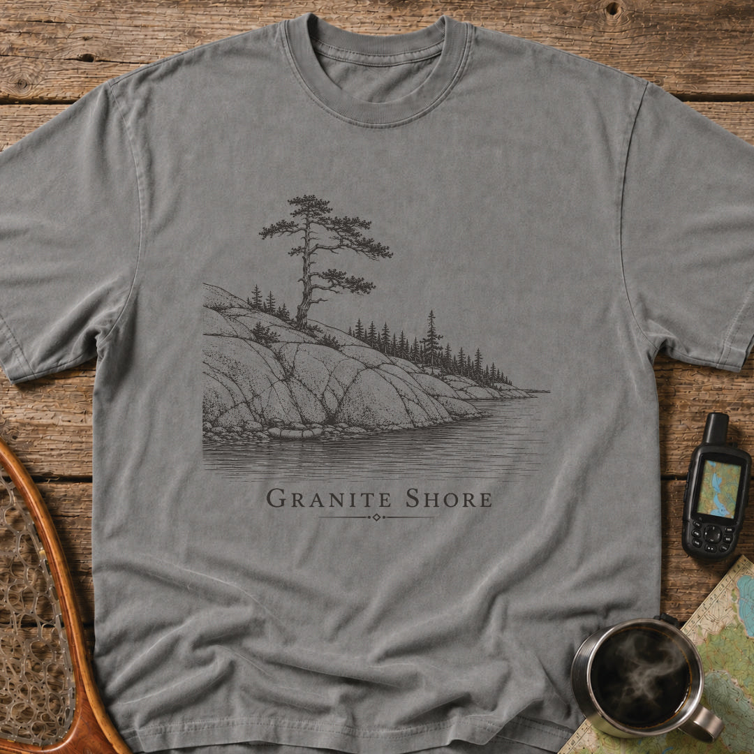 Granite Shore t-shirt featuring a rocky northern shoreline with pine trees overlooking calm wilderness water.