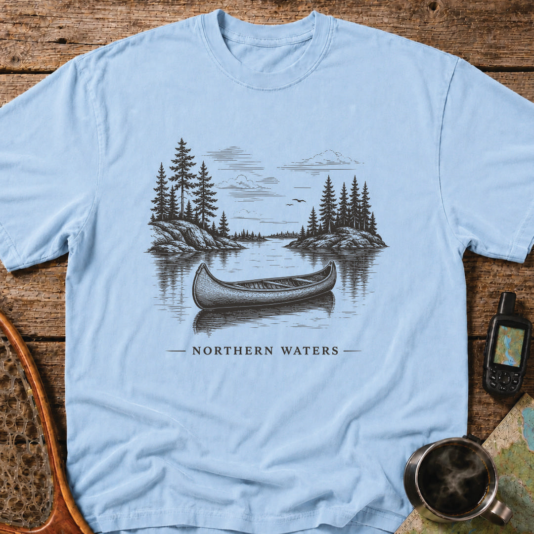 Northern Waters t-shirt featuring a canoe floating on a calm wilderness lake surrounded by pine-covered islands.