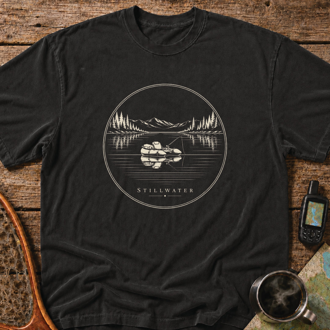 Stillwater t-shirt featuring a packraft floating on a calm mountain lake at sunset.