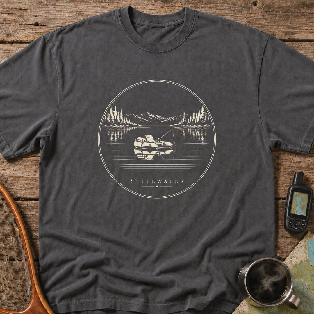 Stillwater t-shirt featuring a packraft floating on a calm mountain lake at sunset.