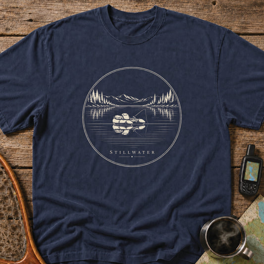 Stillwater t-shirt featuring a packraft floating on a calm mountain lake at sunset.