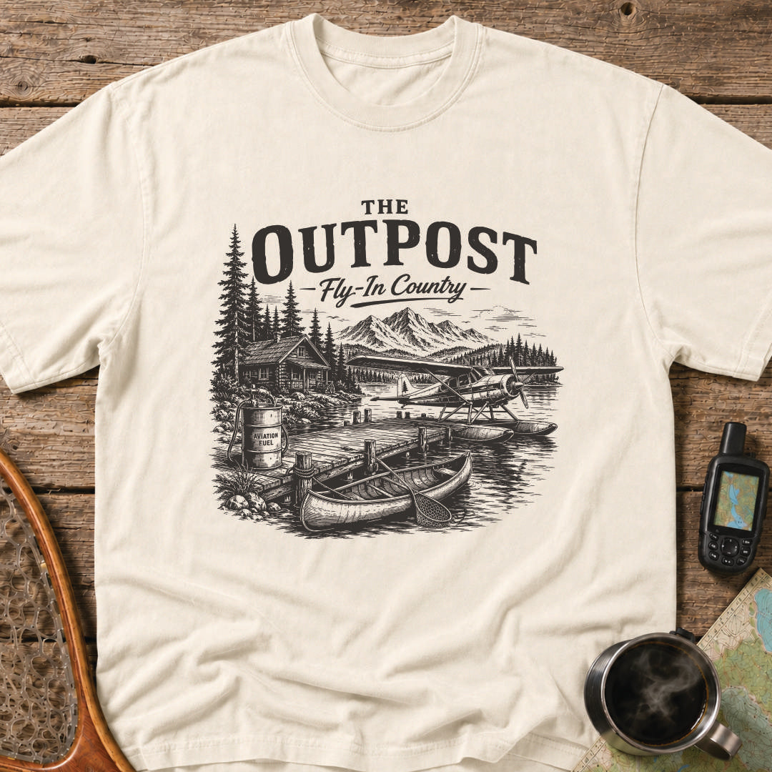 The Outpost Fly-In Country t-shirt featuring a floatplane docked beside a remote fishing lodge and canoe.