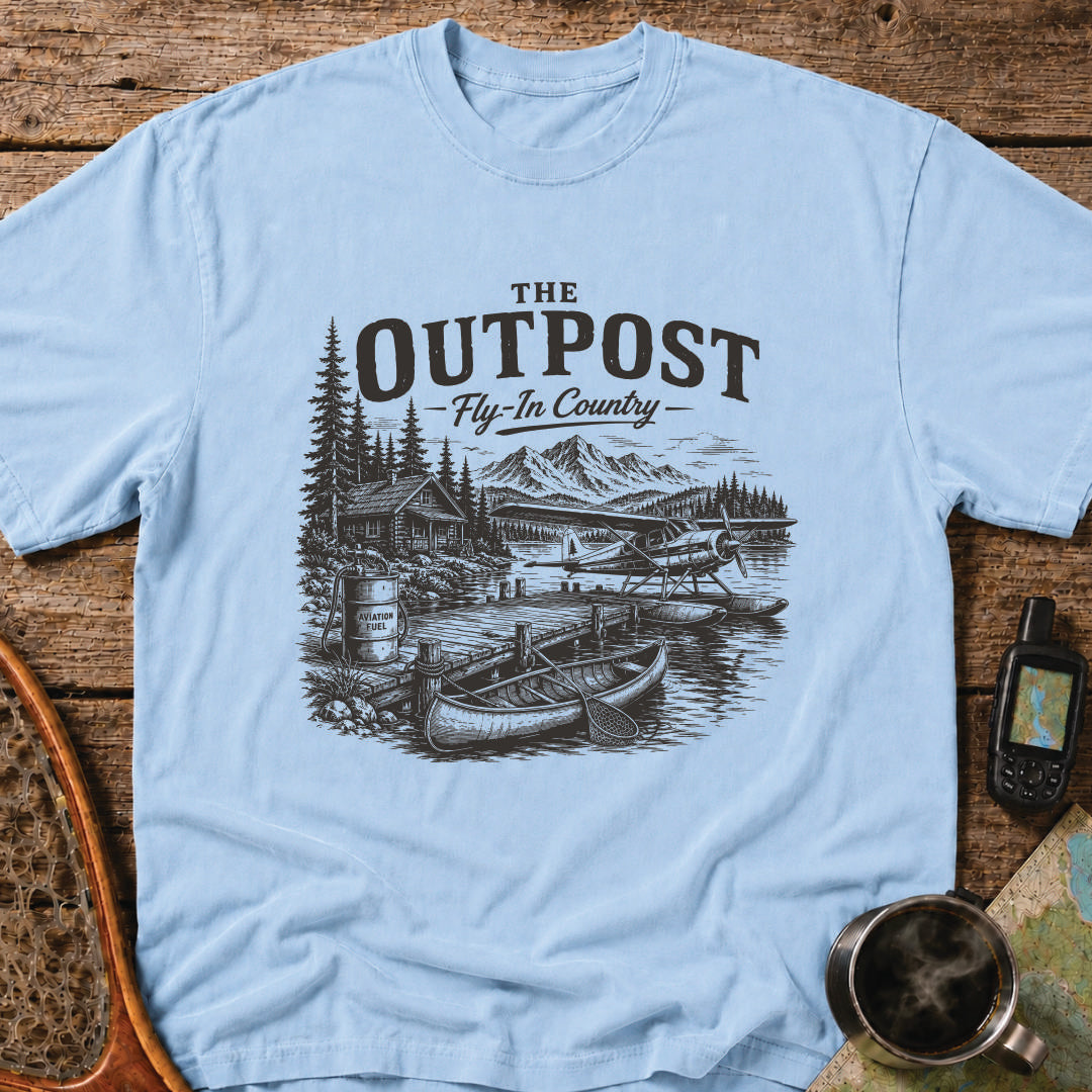 The Outpost Fly-In Country t-shirt featuring a floatplane docked beside a remote fishing lodge and canoe.