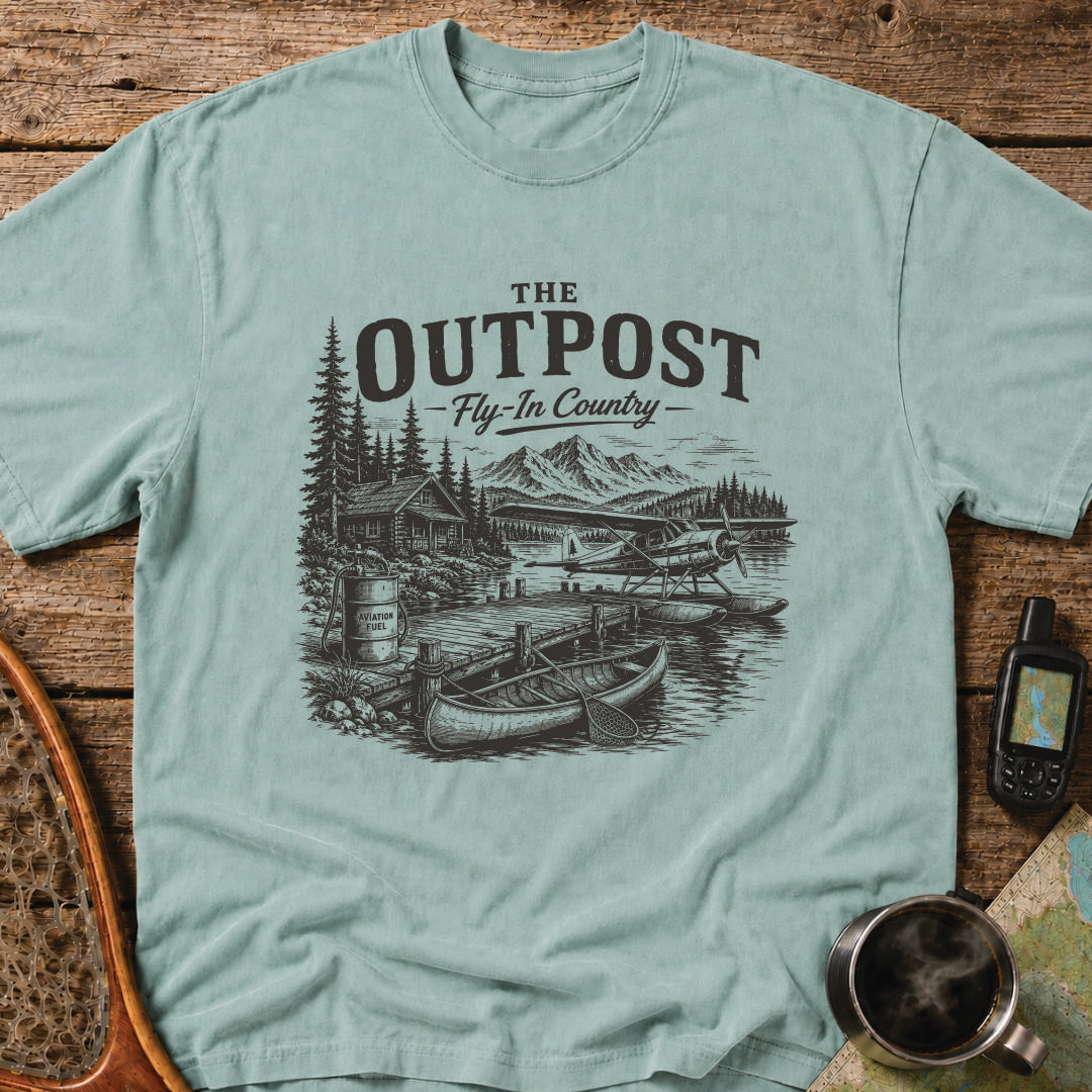 The Outpost Fly-In Country t-shirt featuring a floatplane docked beside a remote fishing lodge and canoe.