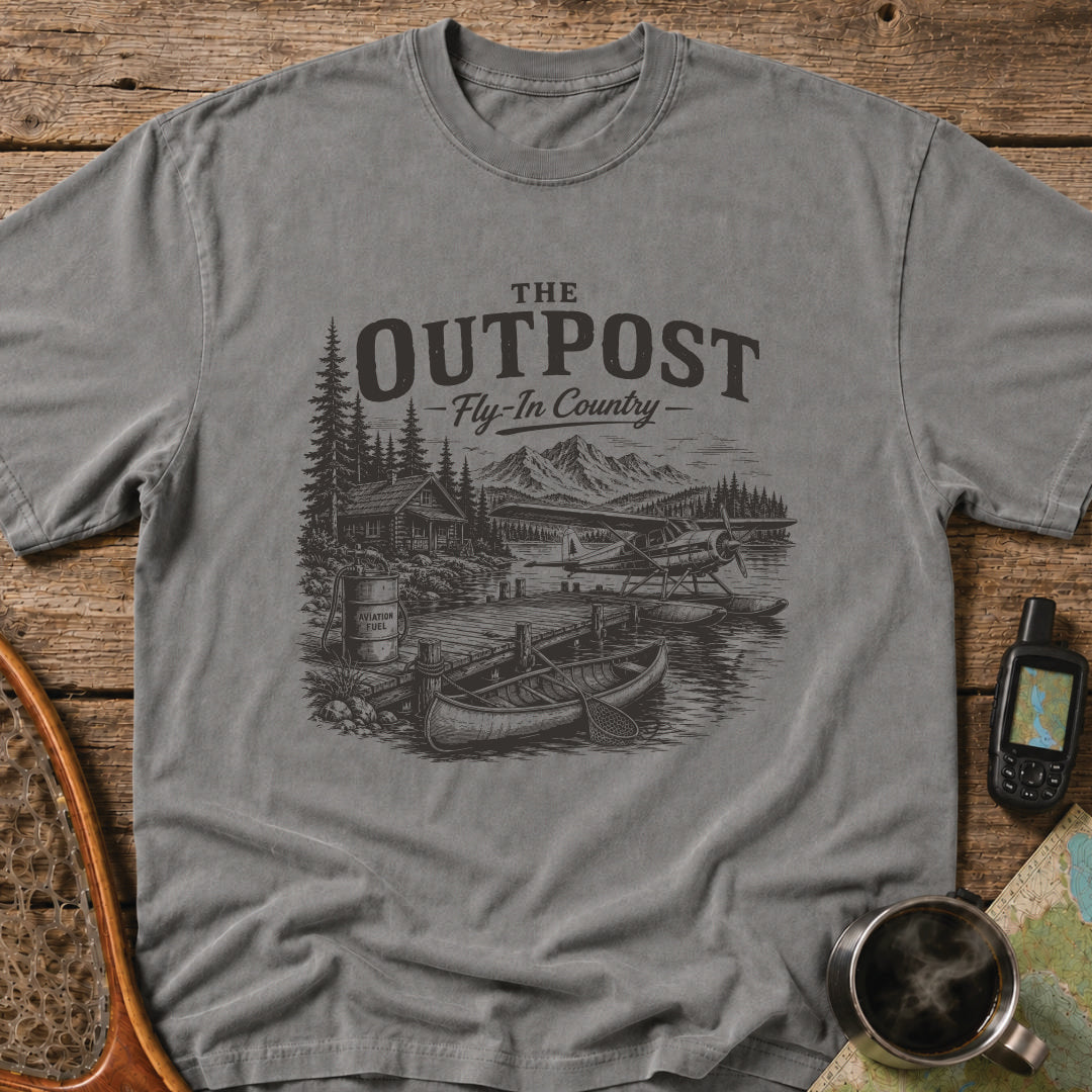 The Outpost Fly-In Country t-shirt featuring a floatplane docked beside a remote fishing lodge and canoe.