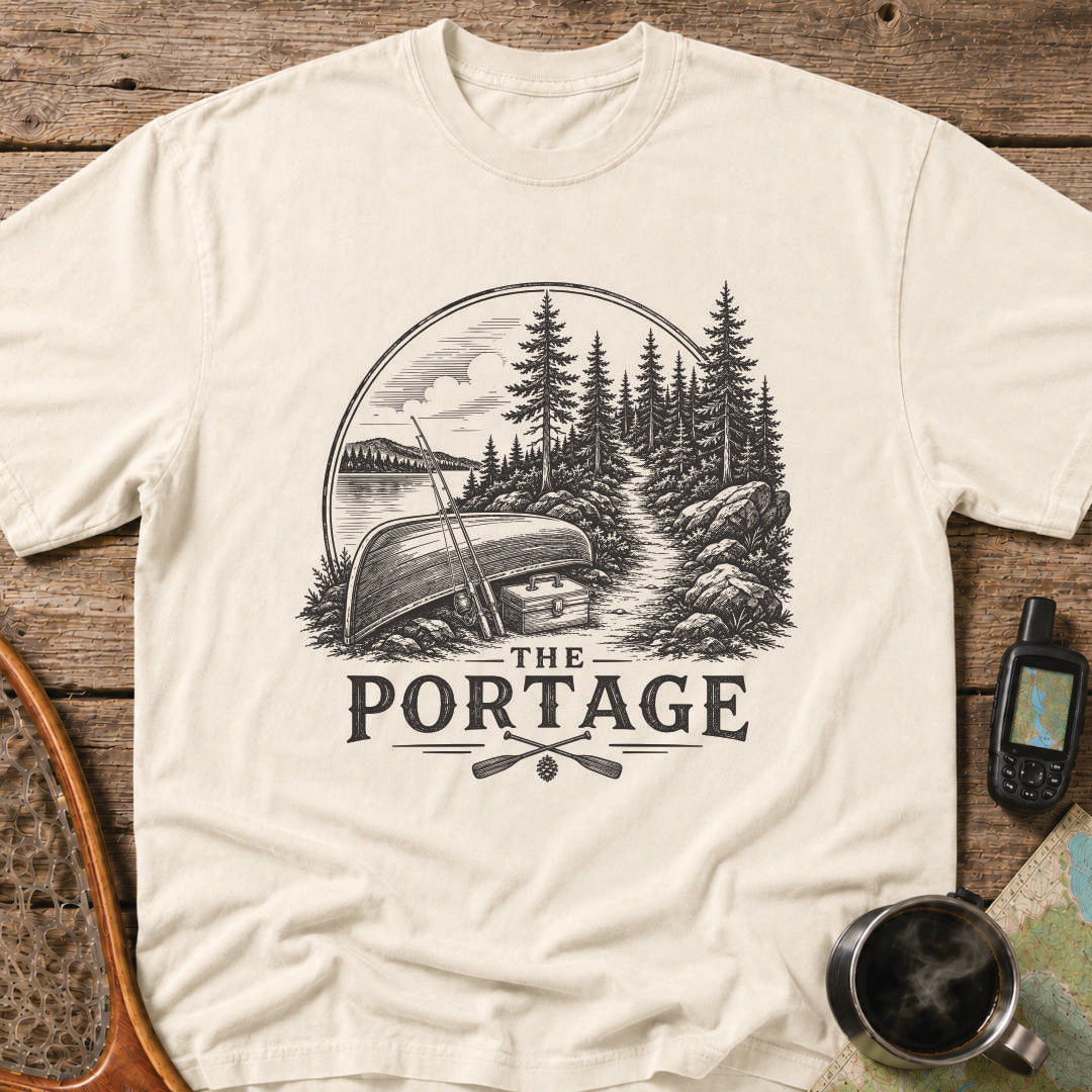 The Portage t-shirt featuring an overturned canoe beside a forest trail with fishing gear.