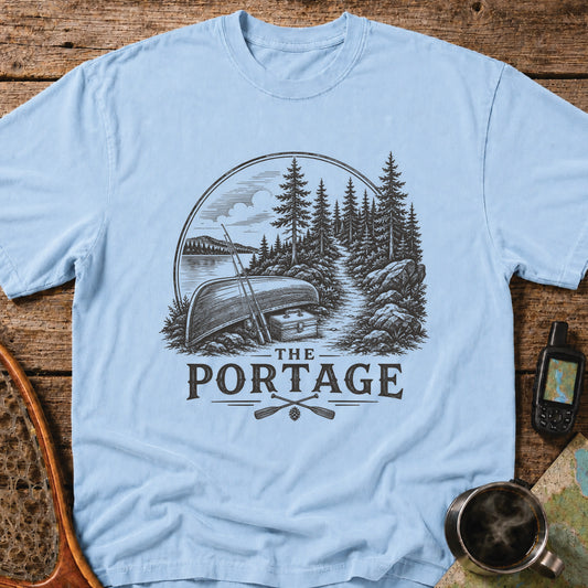 The Portage t-shirt featuring an overturned canoe beside a forest trail with fishing gear.