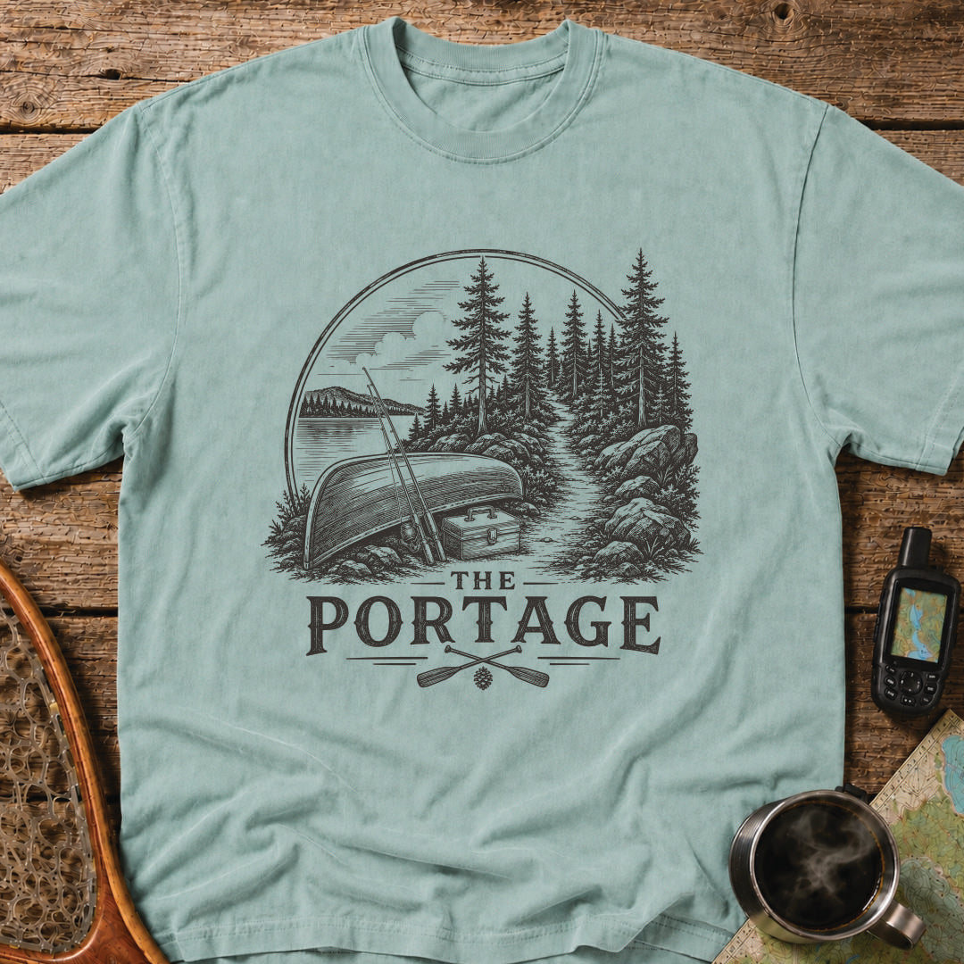 The Portage t-shirt featuring an overturned canoe beside a forest trail with fishing gear.